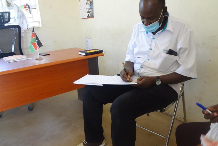 Dr. Romanus Opiyo signs the visitors book at  the Assistant County Commissioner's (ACC) office